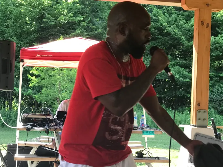 A man in a red shirt rapping into a microphone under the shelter.