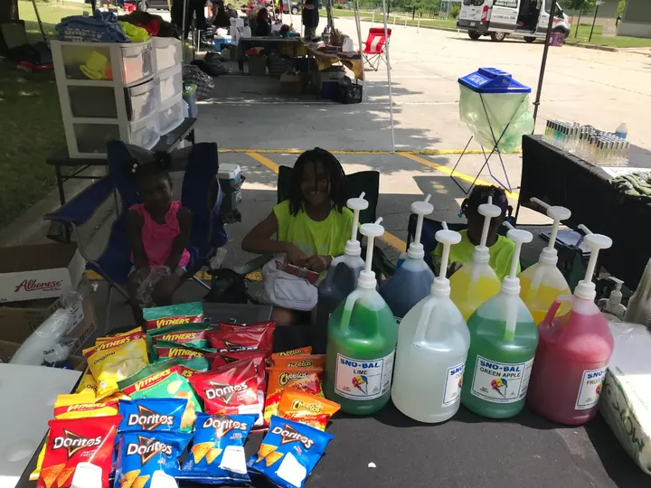A vendor table under a tent with snacks, chips and jugs of drinks.