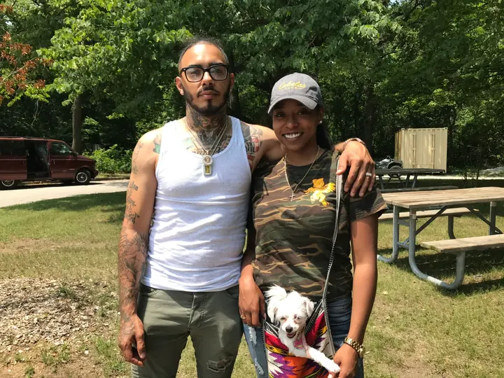 A man and a woman posing in the park with a small dog.