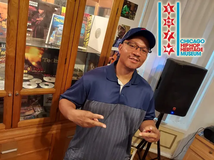 A man in a blue shirt throwing up a hand sign next to a speaker.