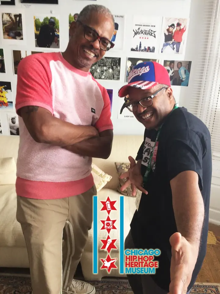 Two men posing in front of framed photos.